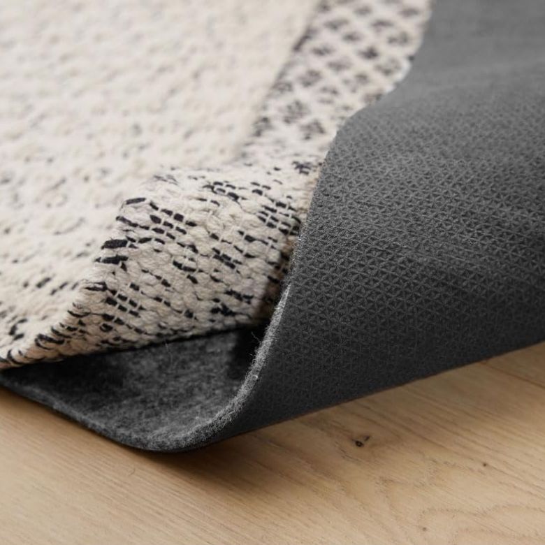 Layered rug corner showing a patterned top rug over a cushioned rug pad on wood flooring.