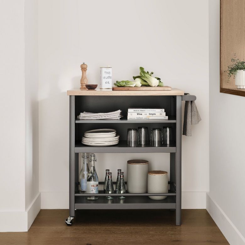 Gray kitchen cart with a wooden top and shelves holding dishes, glasses, and bottles.