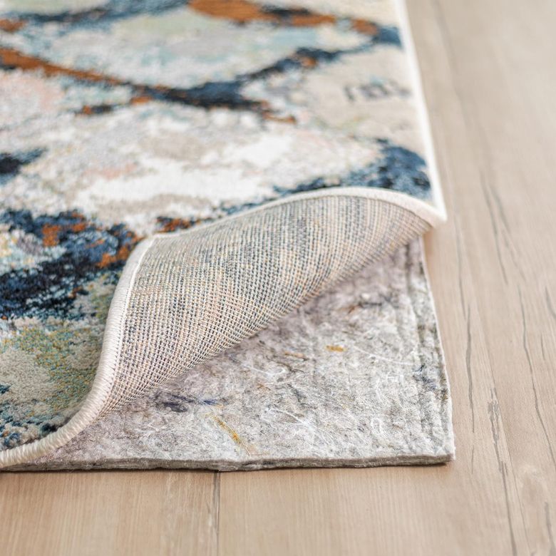 Patterned area rug corner lifted to show the rug pad underneath on a wooden floor.