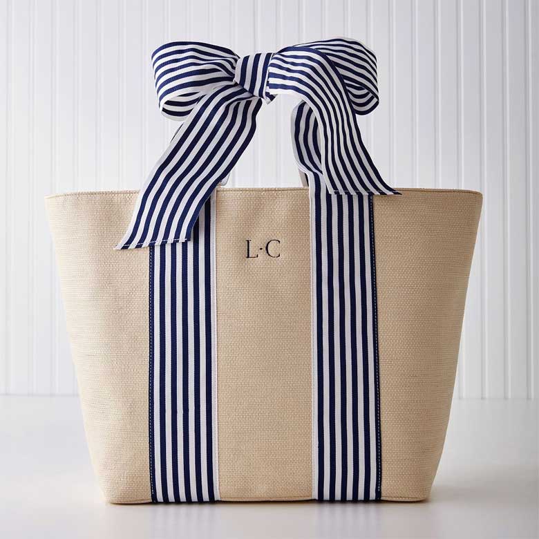Beige tote bag with navy striped handles tied in a bow and monogrammed initials on the front.