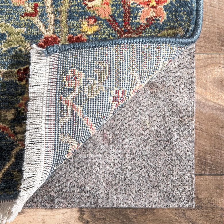 Patterned rug corner lifted to reveal a thick rug pad underneath on a wood floor.