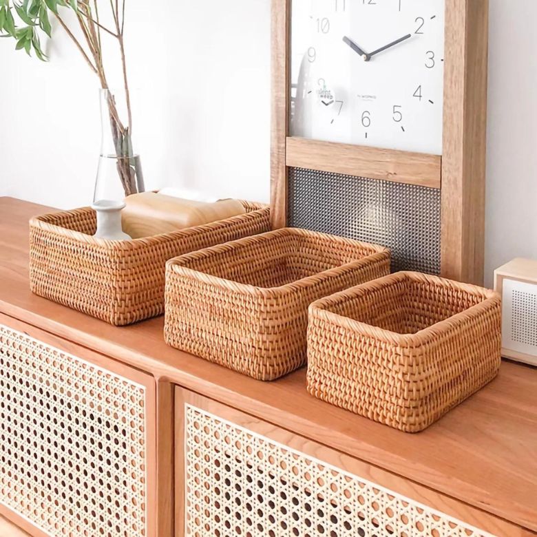 Three woven storage baskets arranged on a wooden cabinet beside a large clock.