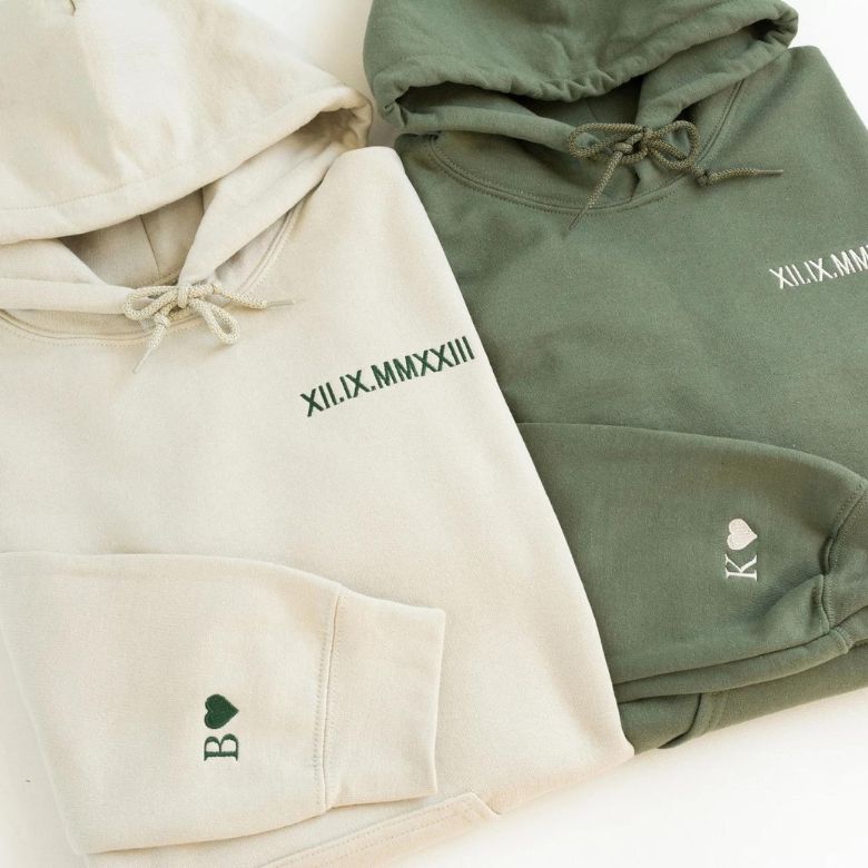 Beige and green hoodies with embroidered Roman numerals and initials with heart symbols.