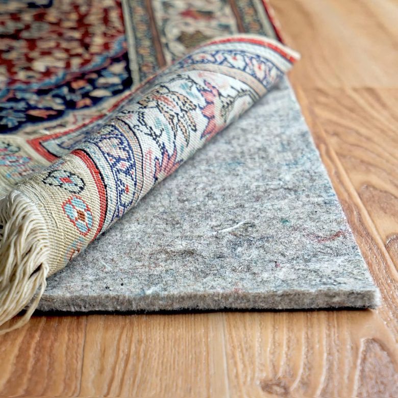 Patterned rug corner rolled to show a thick rug pad underneath on hardwood flooring.