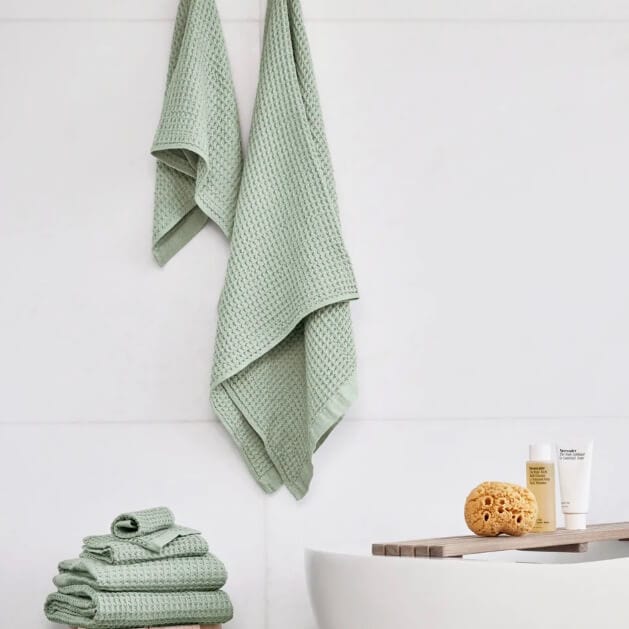Stacked and hanging light green waffle-textured towels in a minimalist bathroom.