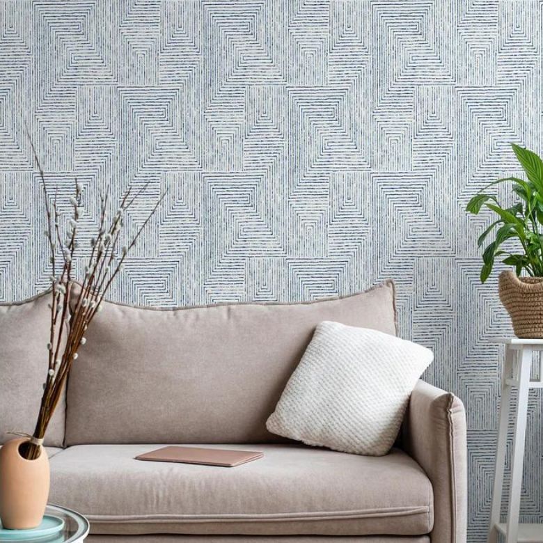 Light beige sofa with a textured pillow in front of a geometric patterned wallpaper and a plant on a side table.