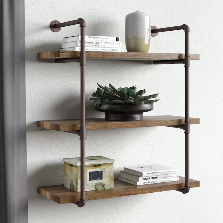 Three-tier wall shelf with wood planks and metal pipe supports decorated with books and vases.