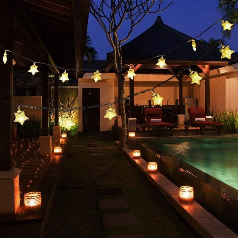 Poolside patio at dusk with glowing star string lights and warm lantern lanterns along the walkway.