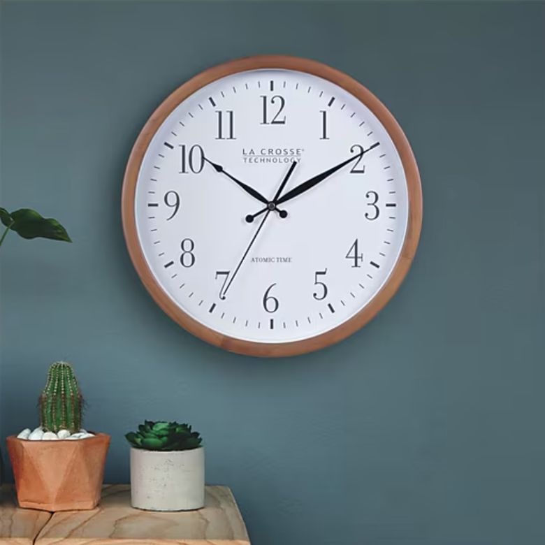 Wall clock with a white face and wooden frame above small potted plants.