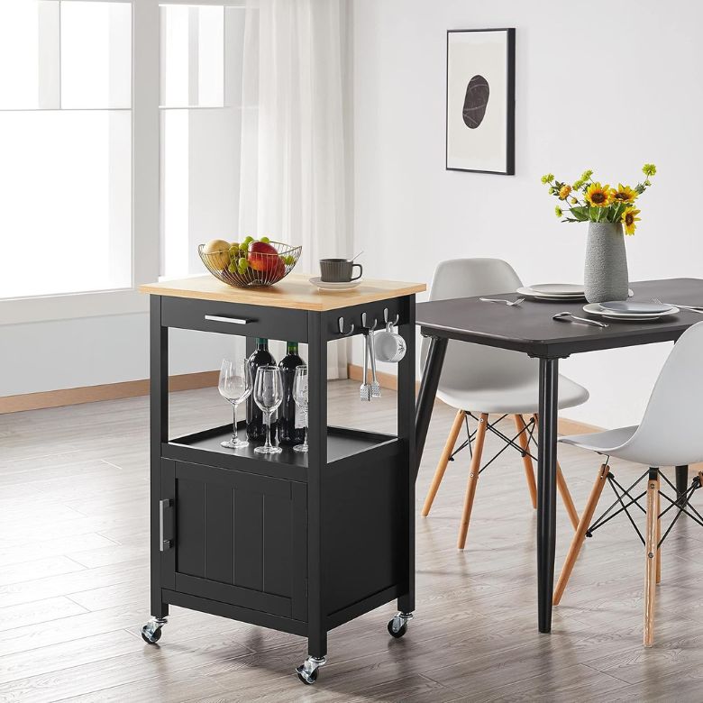 Black rolling kitchen cart with a wood top holding fruit, wine bottles, and glasses beside a dining table.