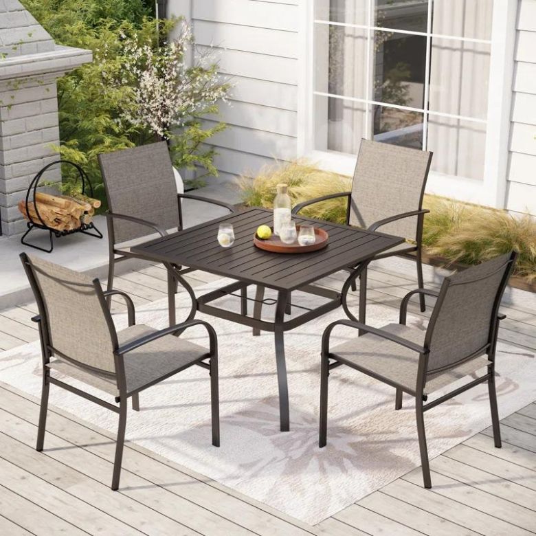 Outdoor dining set with a square table and four mesh chairs on a patio rug.