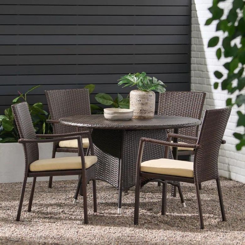 Brown wicker outdoor dining set with a round table and four cushioned chairs on a gravel patio.