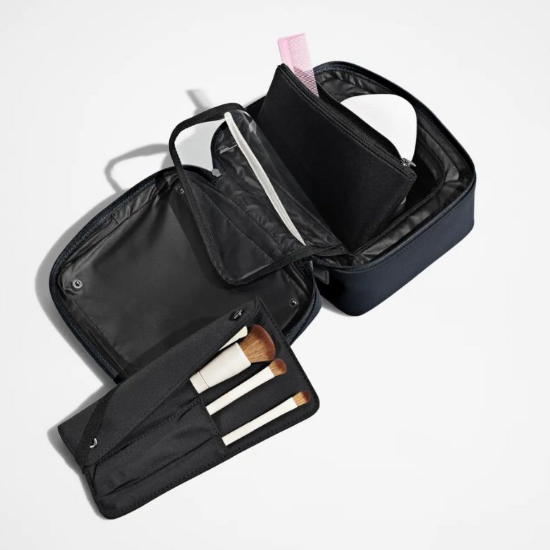Black makeup case opened with brushes, compartments, and a zip pouch.