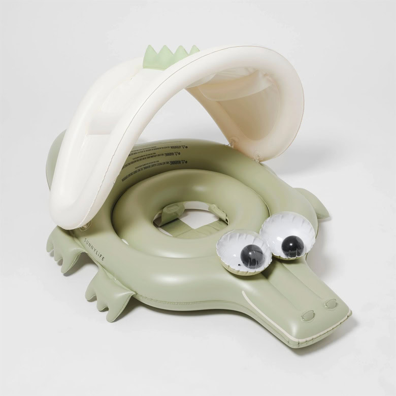 Inflatable green crocodile-shaped baby float with large cartoon eyes and a cream canopy.