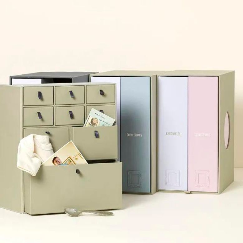 Stacked keepsake storage boxes with small drawers and pastel binders holding baby mementos and photos.