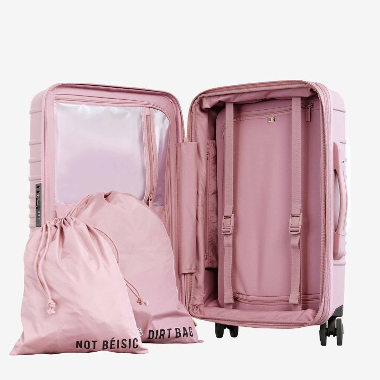 Open pink hard-shell suitcase with interior compartments and matching drawstring laundry bags.