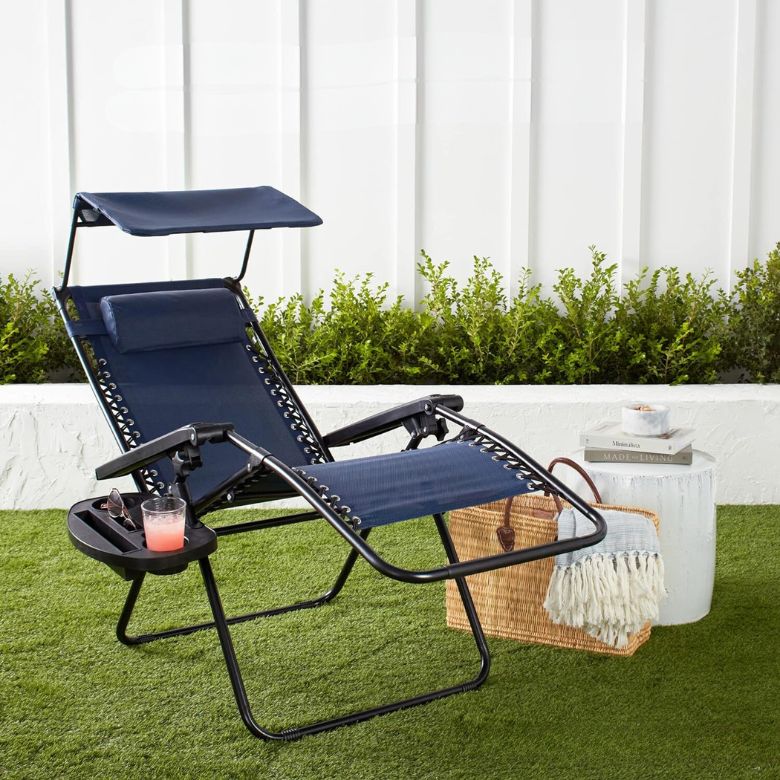 Navy blue reclining outdoor lounge chair with canopy and side tray on a grassy patio setup.