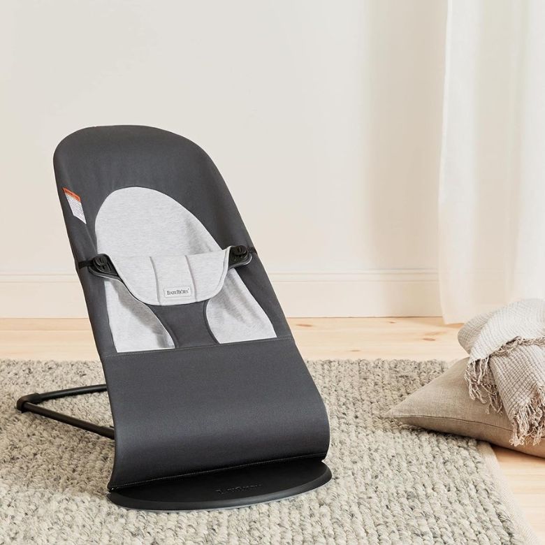 Gray baby bouncer seat placed on a textured rug in a softly lit room.