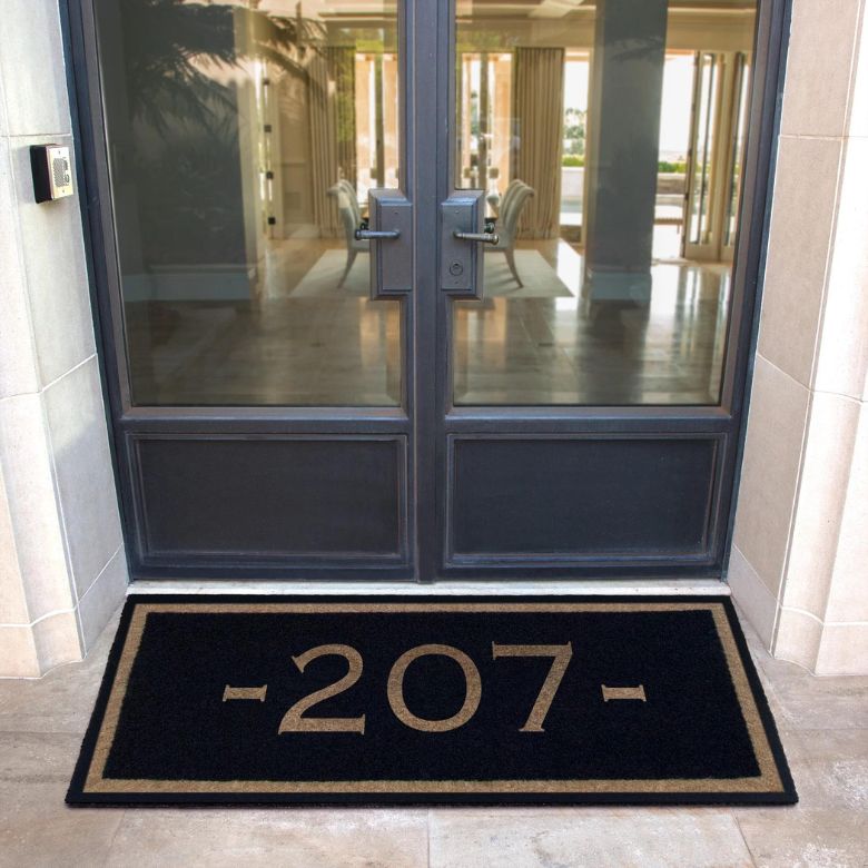 Black doormat with the number 207 placed in front of a glass double door.