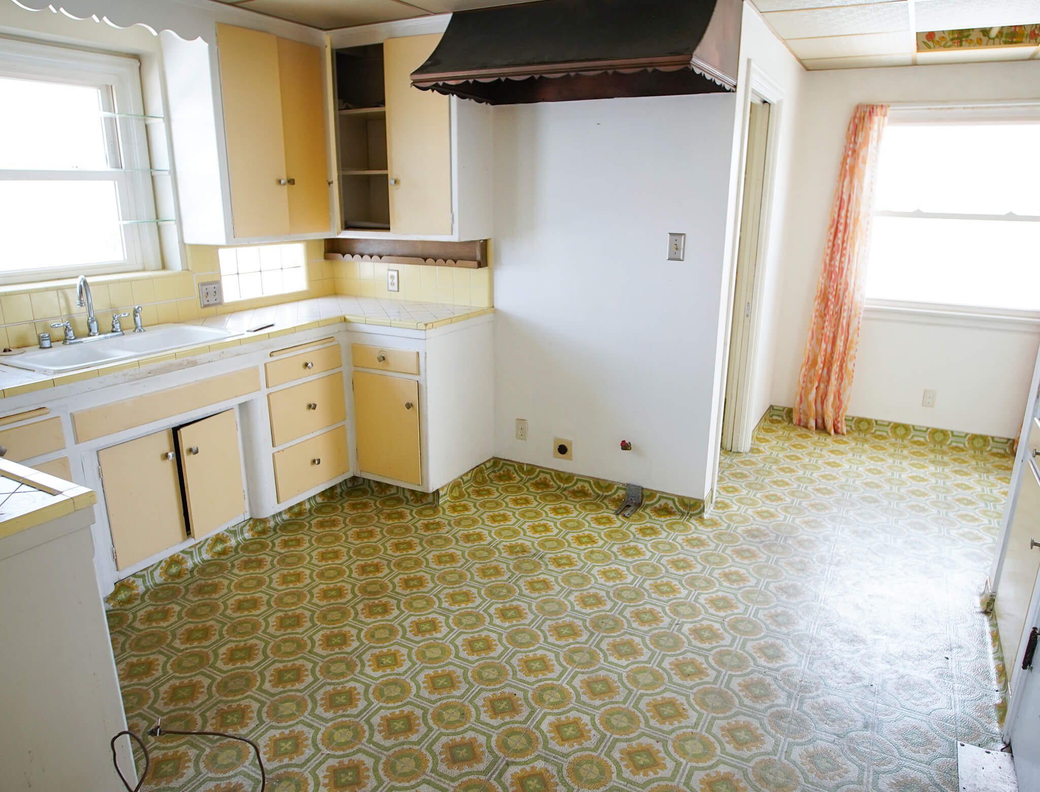 old, yellowed, and outdated kitchen area with empty cabinets and no appliances