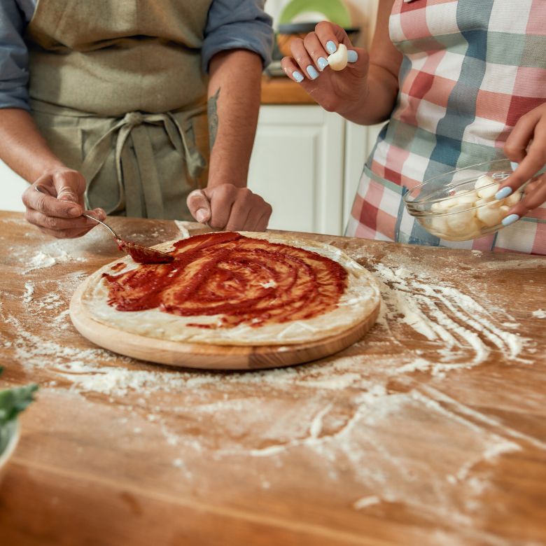 a man and woman making a pizza at home