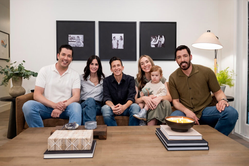 courteney cox celebrity iou episode with the property brothers hosts drew and jonathan scott, posing on a couch with friends marisa, annie, and baby june