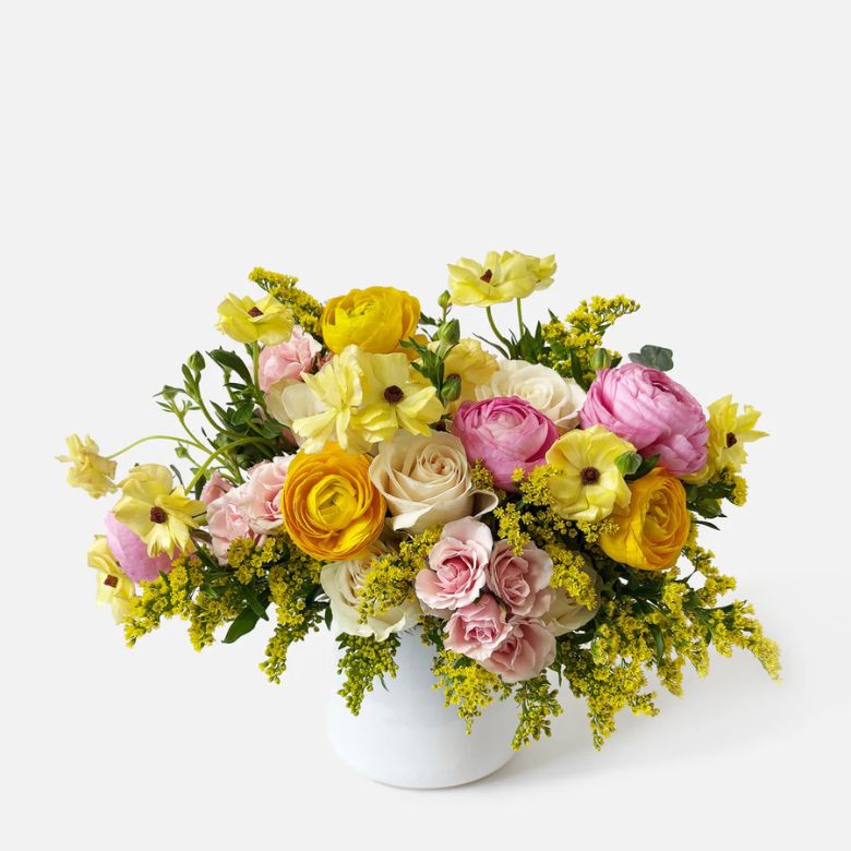 Multi-colored Roses, Ranunculus and Solidago flower arrangement in a white ceramic vase.