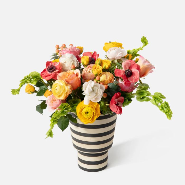 Multi-colored Rose, Ranunculus and Anemone flower arrangement in a striped ceramic vase.