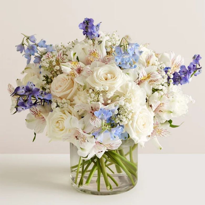 floral arrangement with white roses, carnations and Peruvian lilies; blue delphinium; baby’s breath and assorted greenery