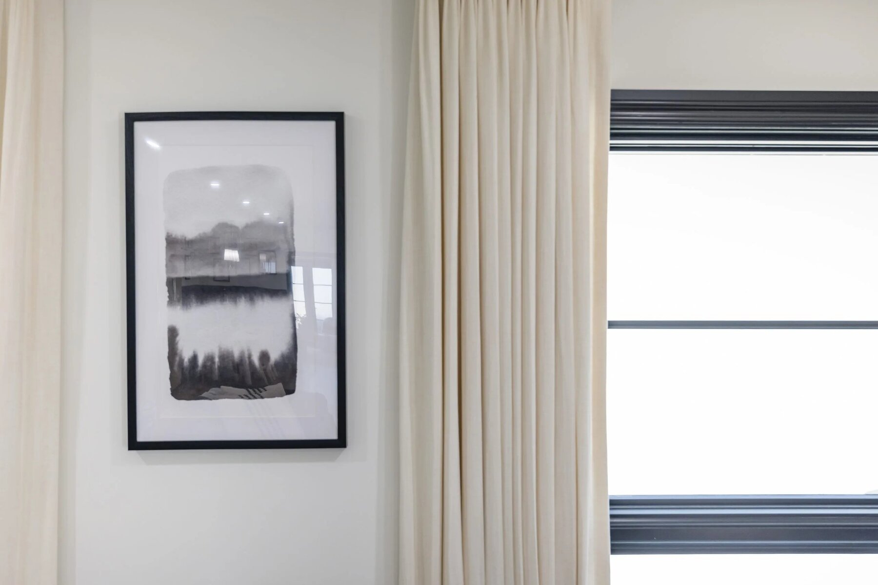 Minimalist interior with framed abstract artwork cream curtains and black window trim