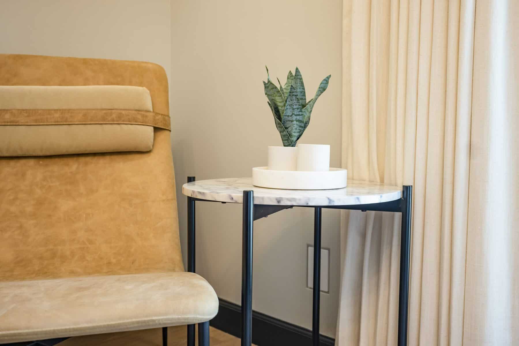 Tan leather chair beside a marble-top side table with a small potted plant