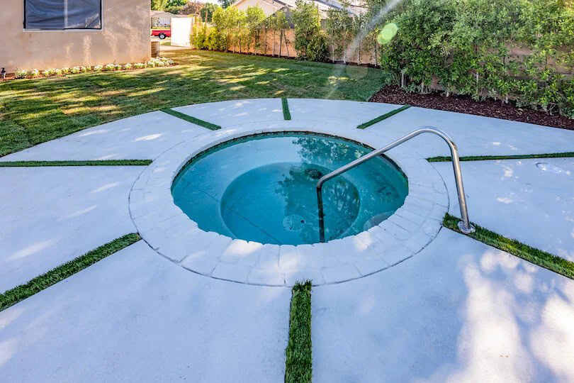 Circular backyard hot tub with white concrete surround and grass inlays