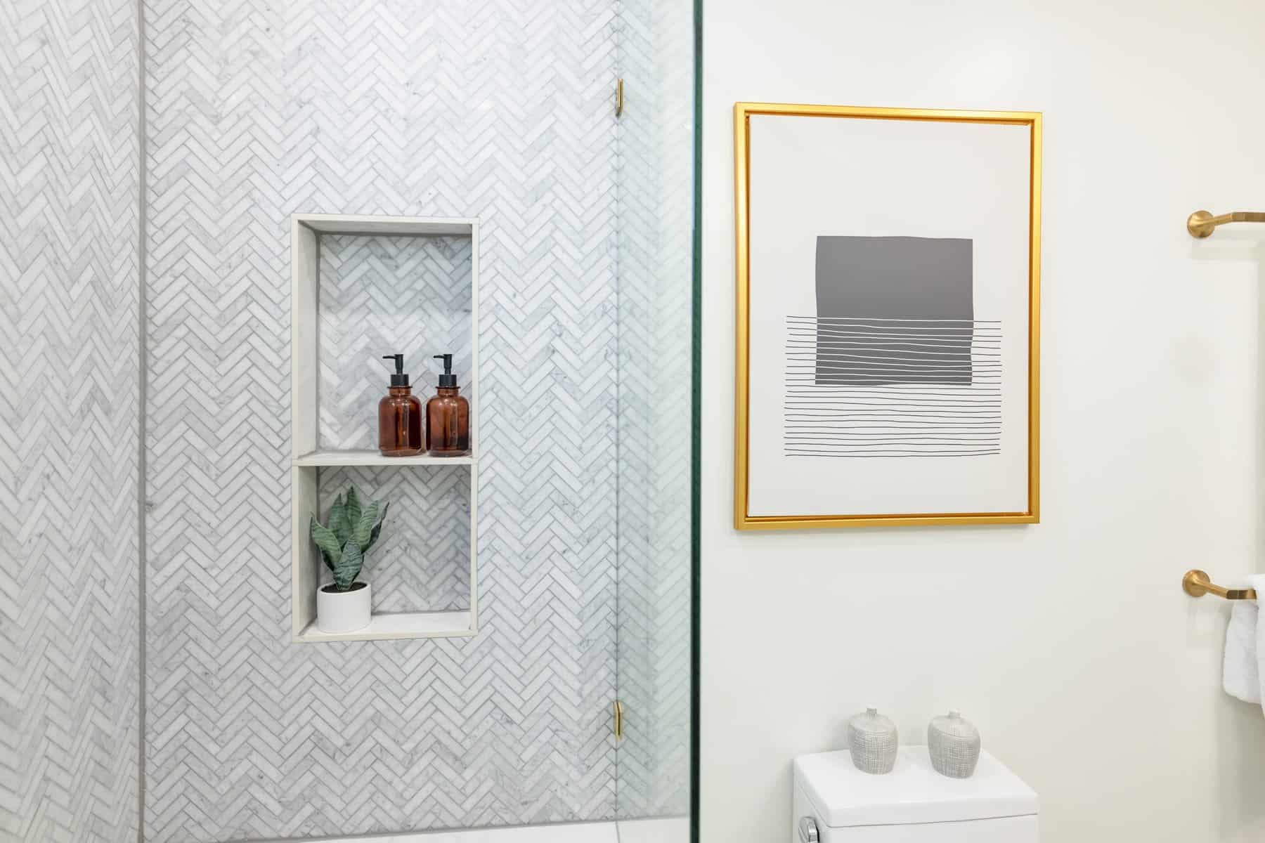 Marble shower with shelf, amber bottles, and wall art above toilet