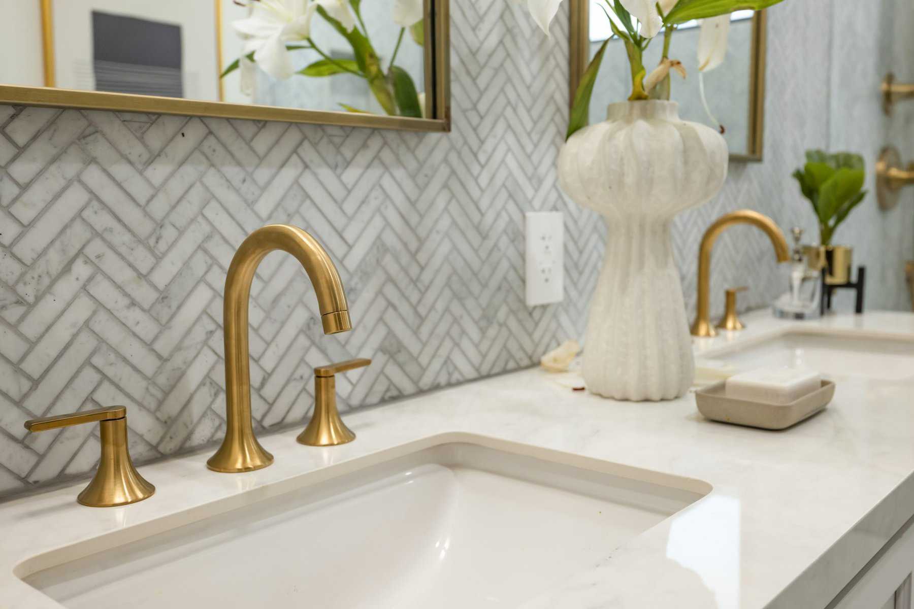 Bathroom vanity with gold faucets, marble countertop, and decorative vase