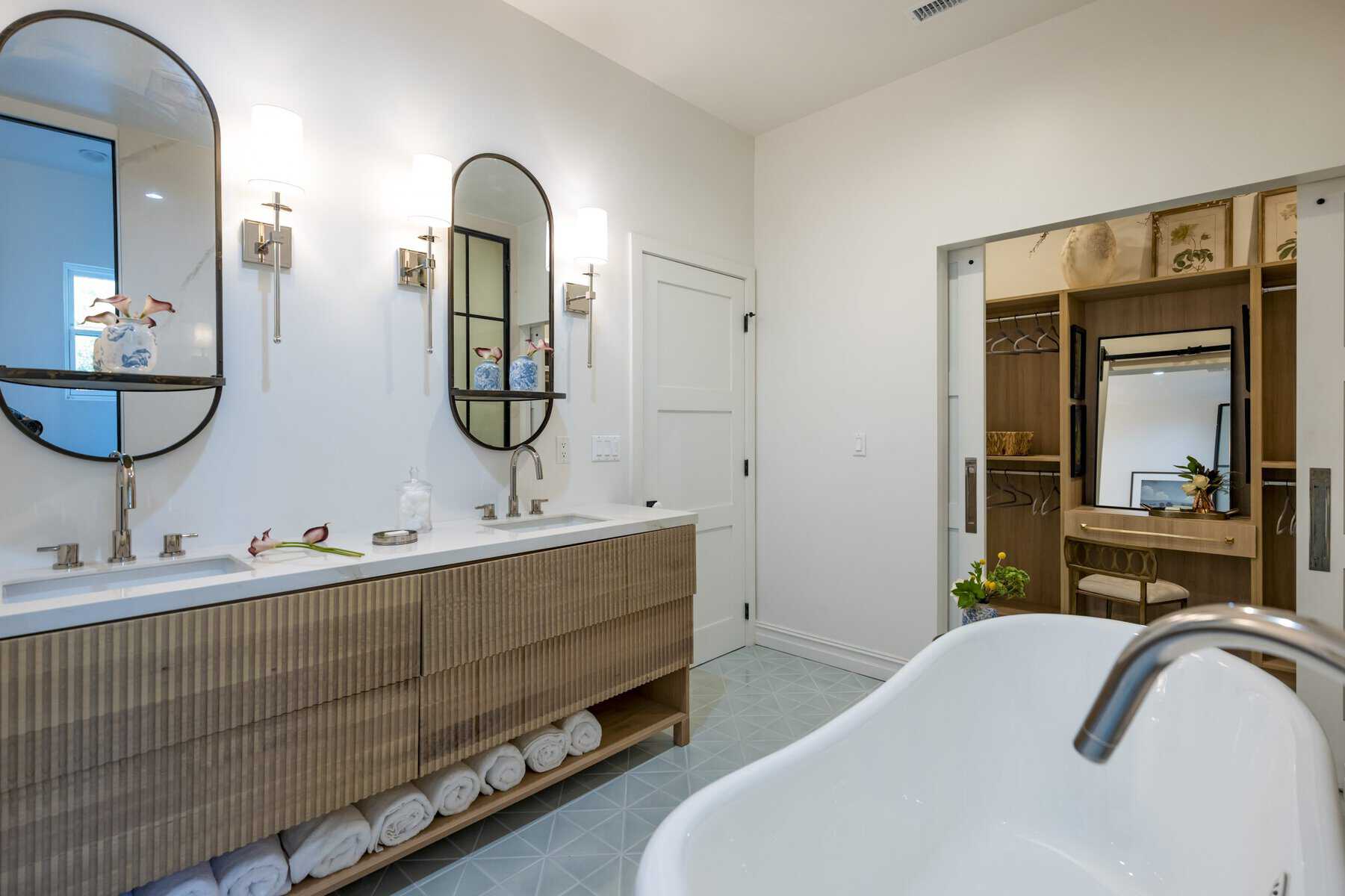 Bathroom with double vanity, oval mirrors, freestanding bathtub, and walk-in closet