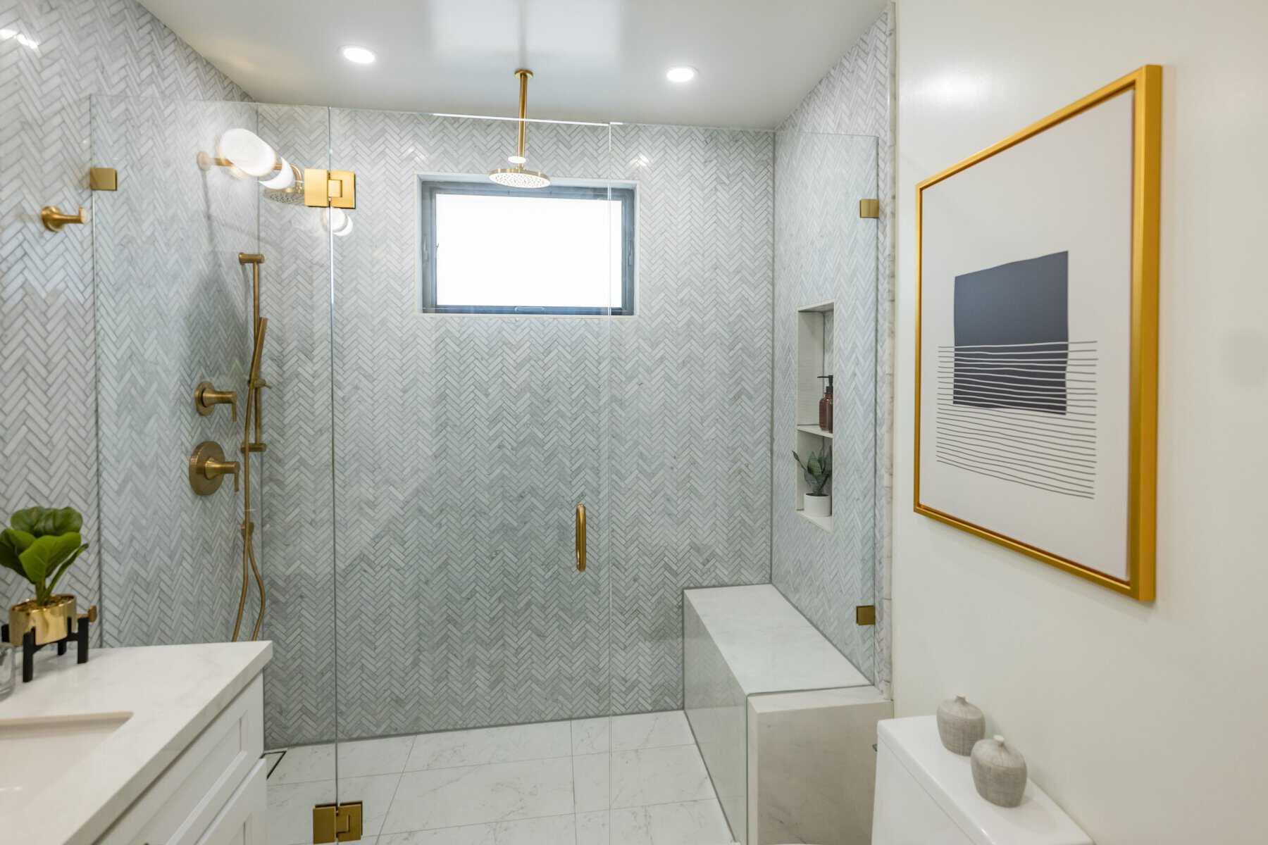 Modern bathroom with a glass-enclosed shower, gold fixtures, herringbone tile, and a built-in bench