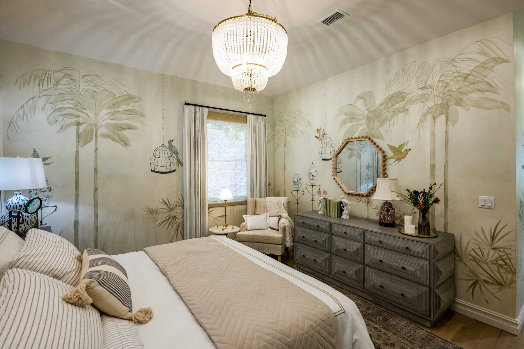 Cozy bedroom with palm tree wall murals, a chandelier, a gray dresser, and a beige armchair