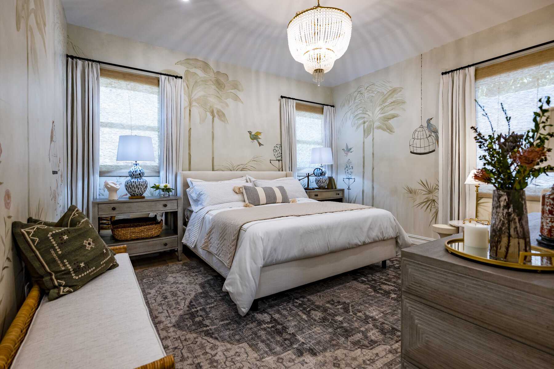 Elegant bedroom with a chandelier, hand-painted nature-themed walls, and cozy neutral decor