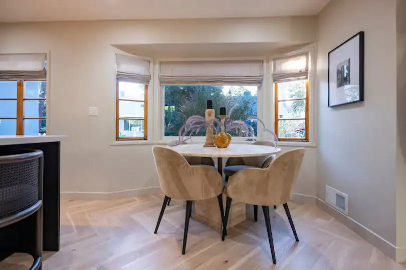 Small dining nook with beige velvet chairs and a round table by bay windows