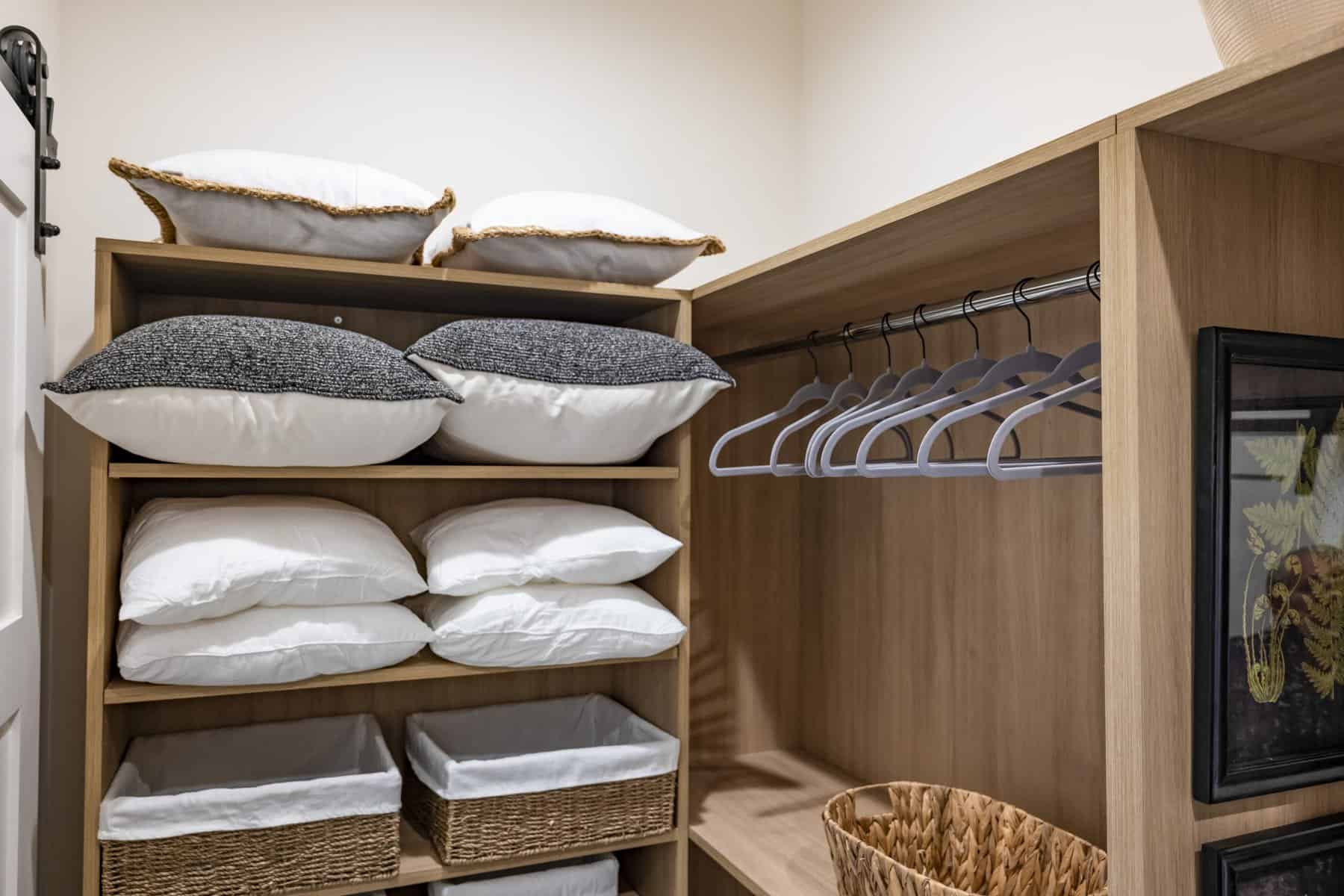 Organized closet with pillows, wicker baskets, and hanging space with hangers