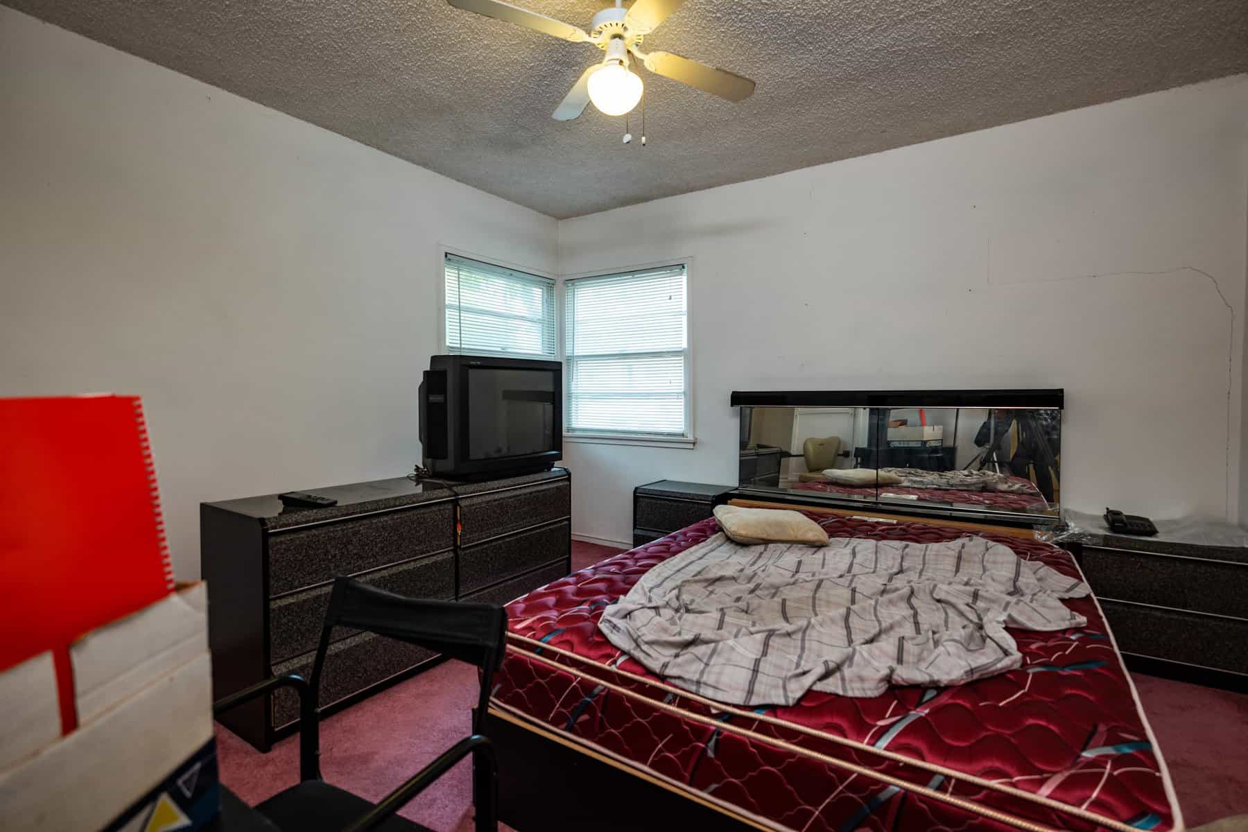 Cluttered bedroom with an unmade bed, old box TV on a dresser, mirrored headboard, and pink carpet