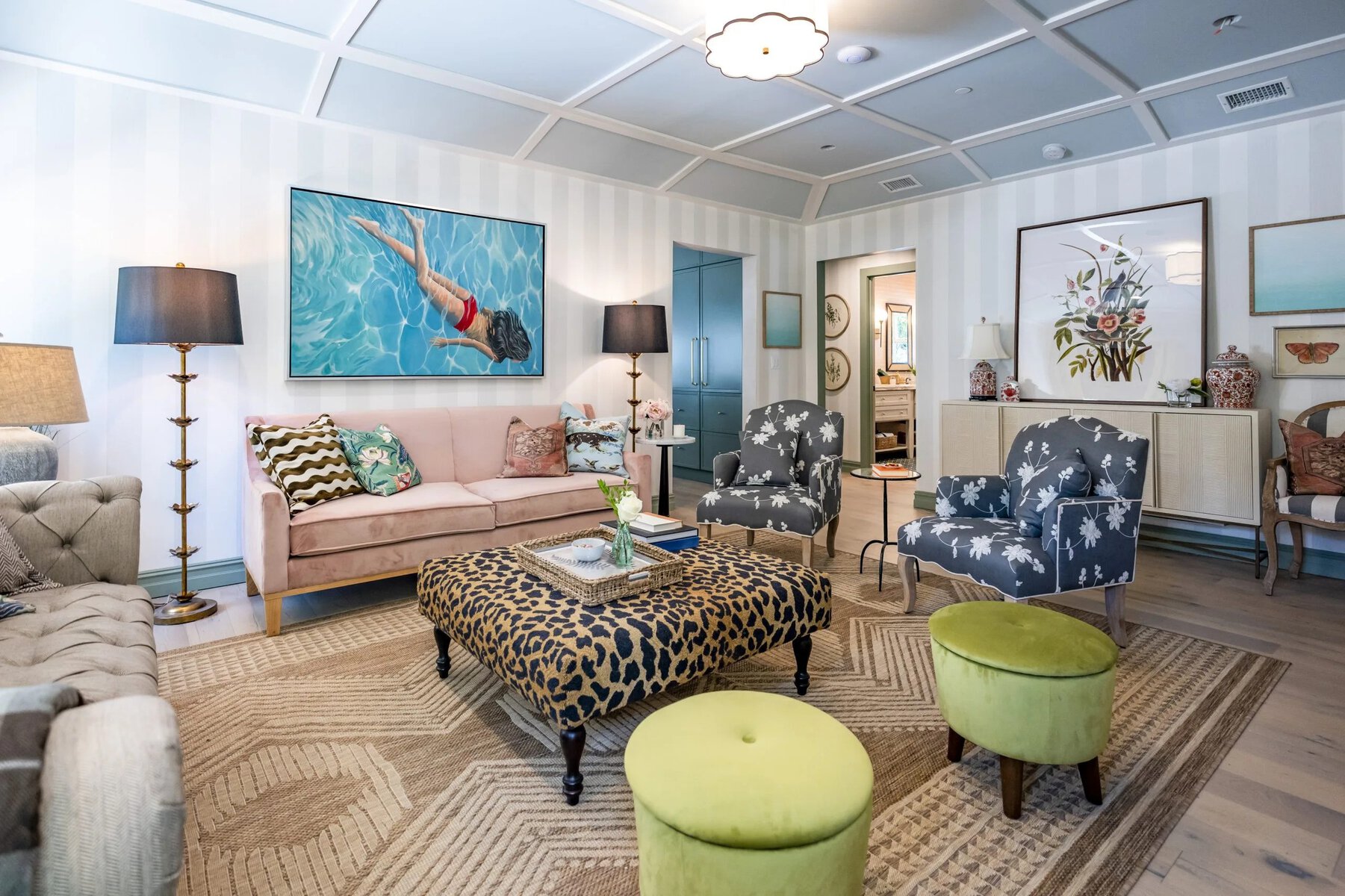 Eclectic living room with a pink sofa, floral chairs, leopard ottoman, and green stools under a coffered ceiling
