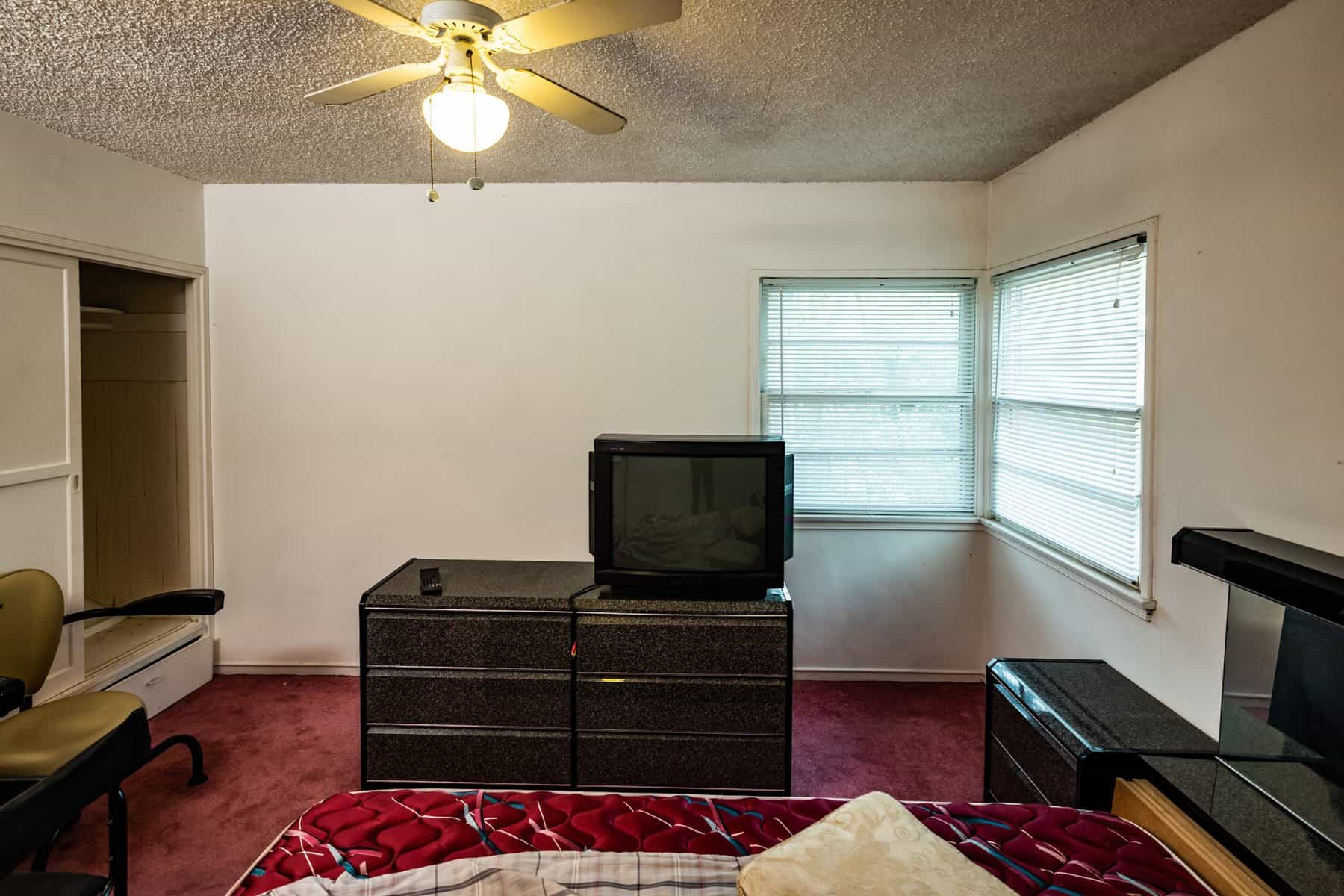 Dated bedroom with a ceiling fan, old television, and red carpet flooring