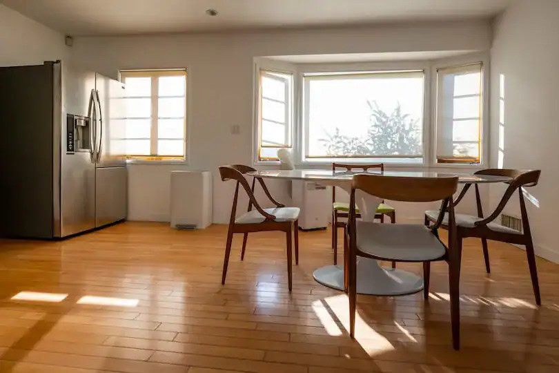Bright dining area with a round table, wooden chairs, and large bay windows