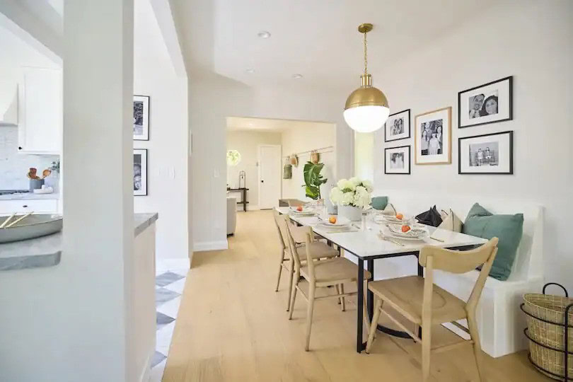 Bright dining area with a white table, wood chairs, built-in bench seating, and gallery wall of family photos