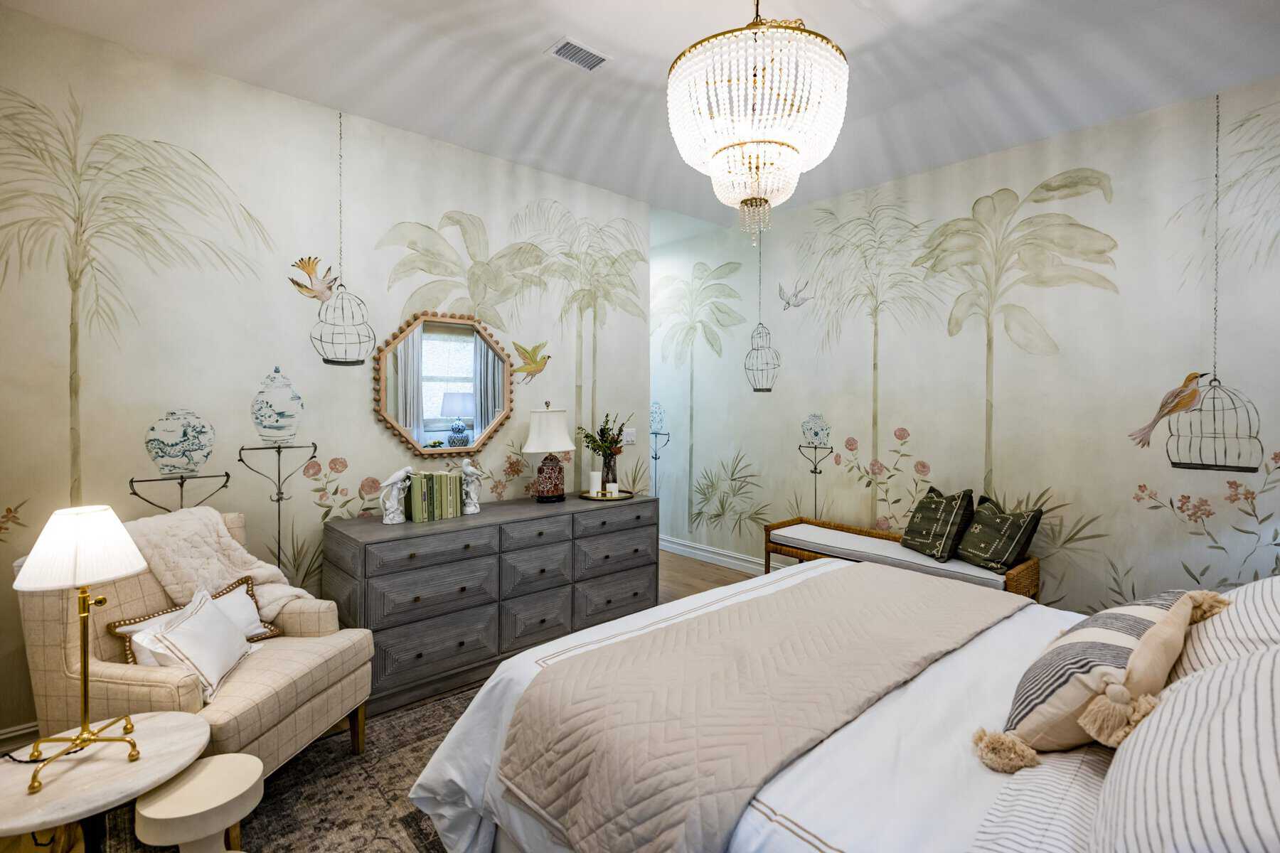 Bedroom with tropical wallpaper, a large double bed with white bedding, a dresser, a chair, and chandelier