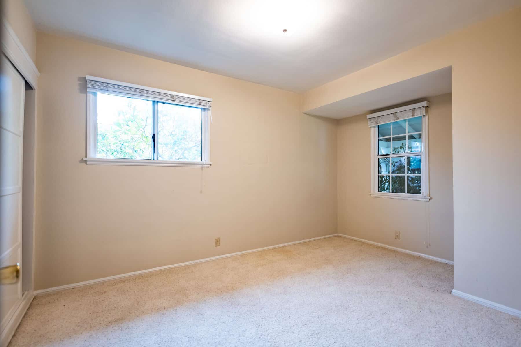 Empty beige bedroom with carpet flooring and two windows