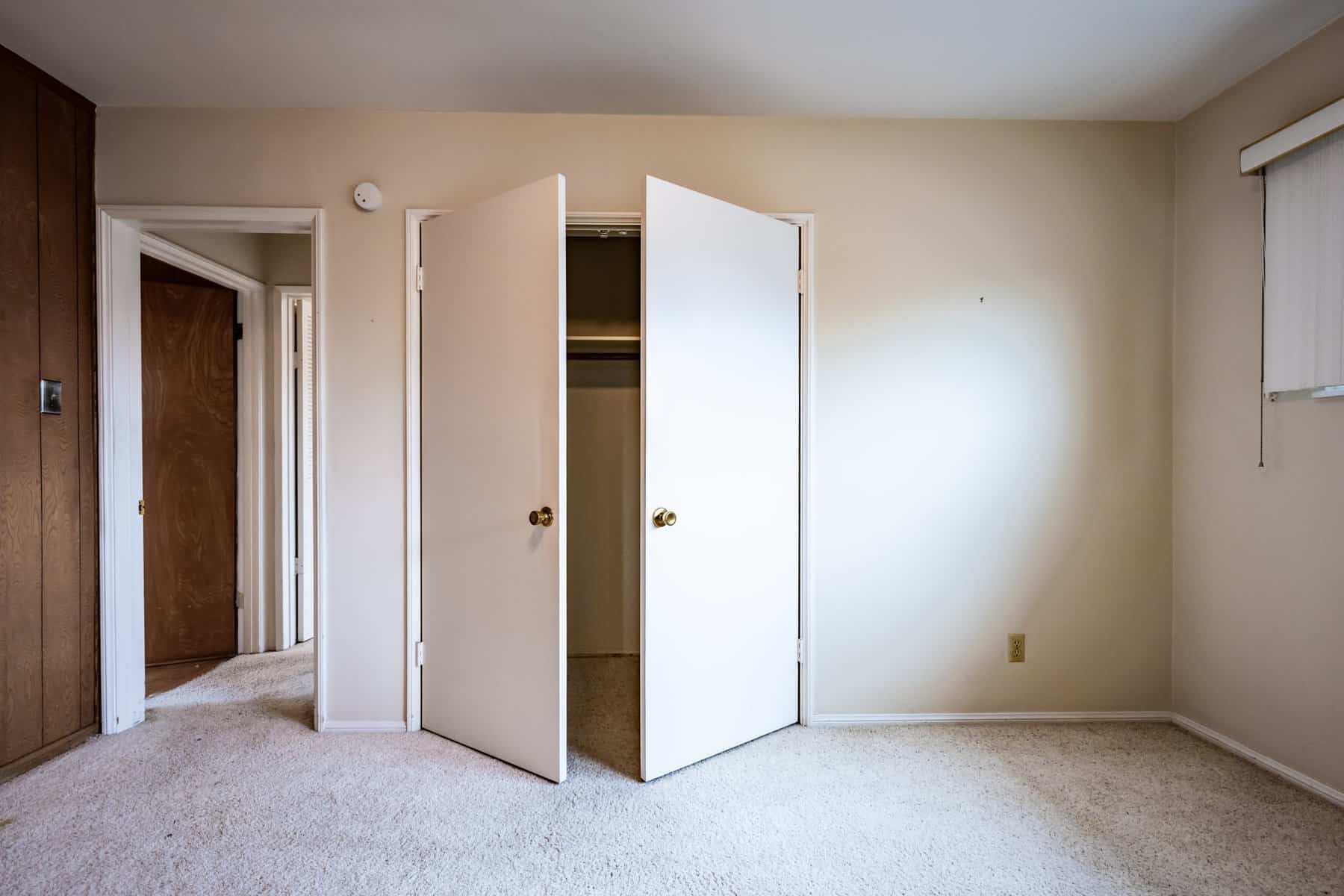 Minimalist bedroom with open closet doors, beige carpet, and wood-paneled accent wall