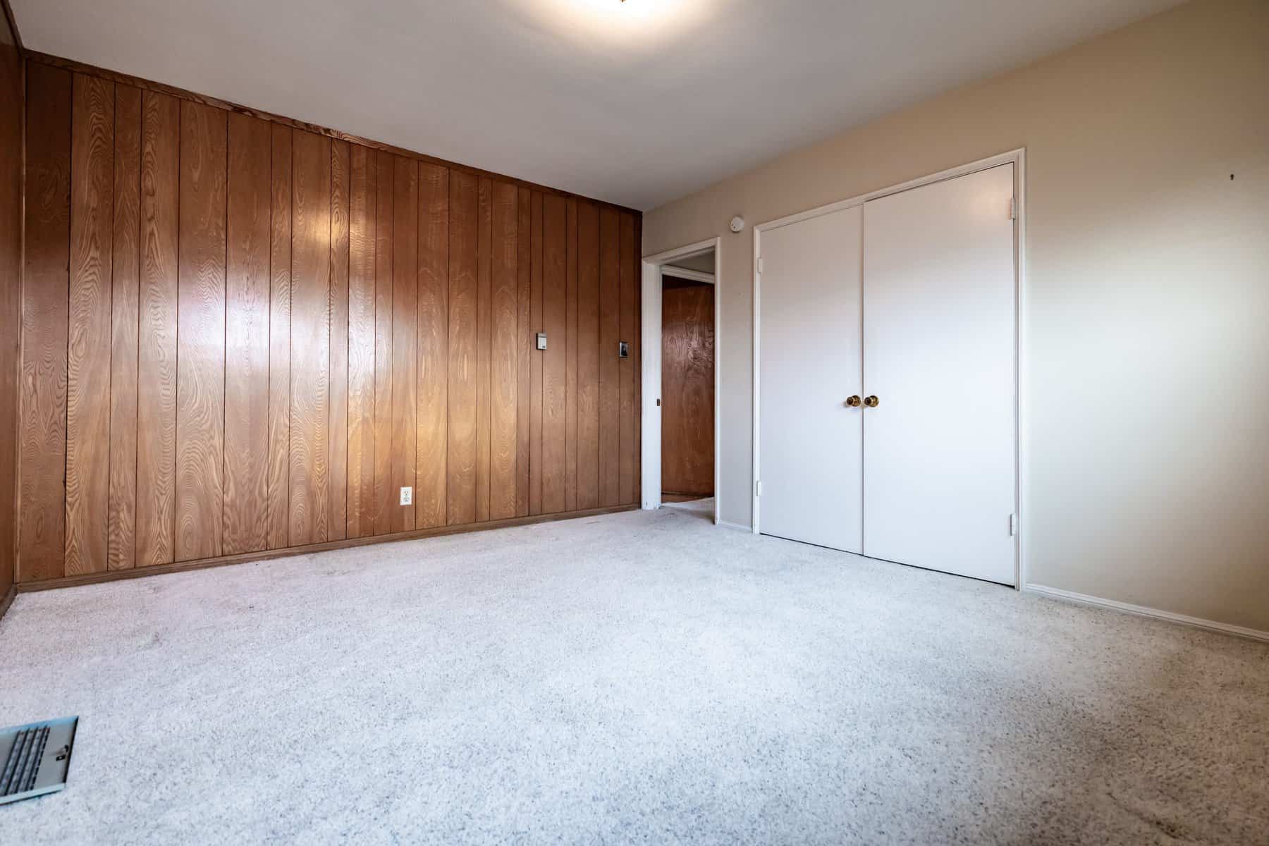 Empty room with wood panel accent wall, white closet doors, and light carpet flooring