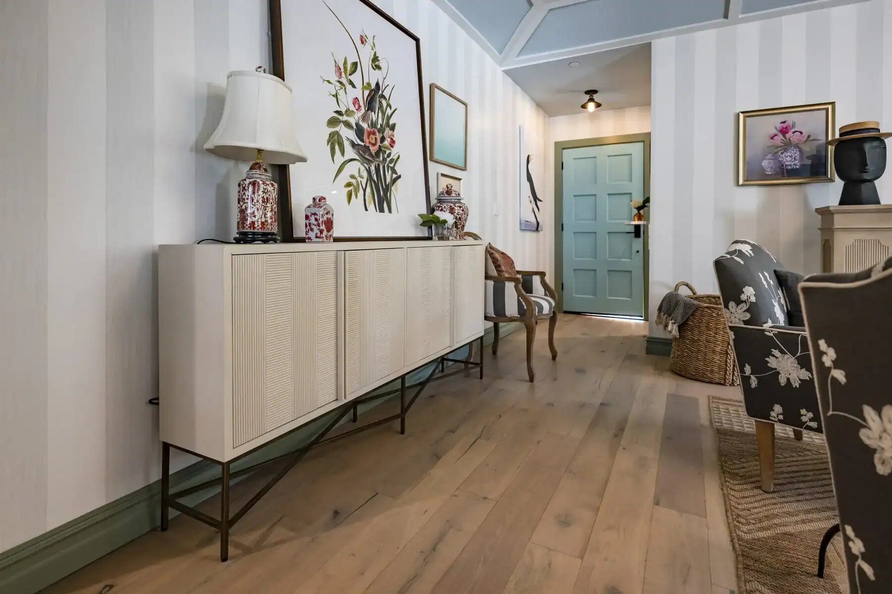 Entryway with striped wallpaper, sideboard, floral artwork, and blue front door